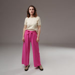 Pantaloni evazați din viscoză fucsia, talie elastică și cordon lat, model lejer, purtați cu un top crem, vedere frontală completă.