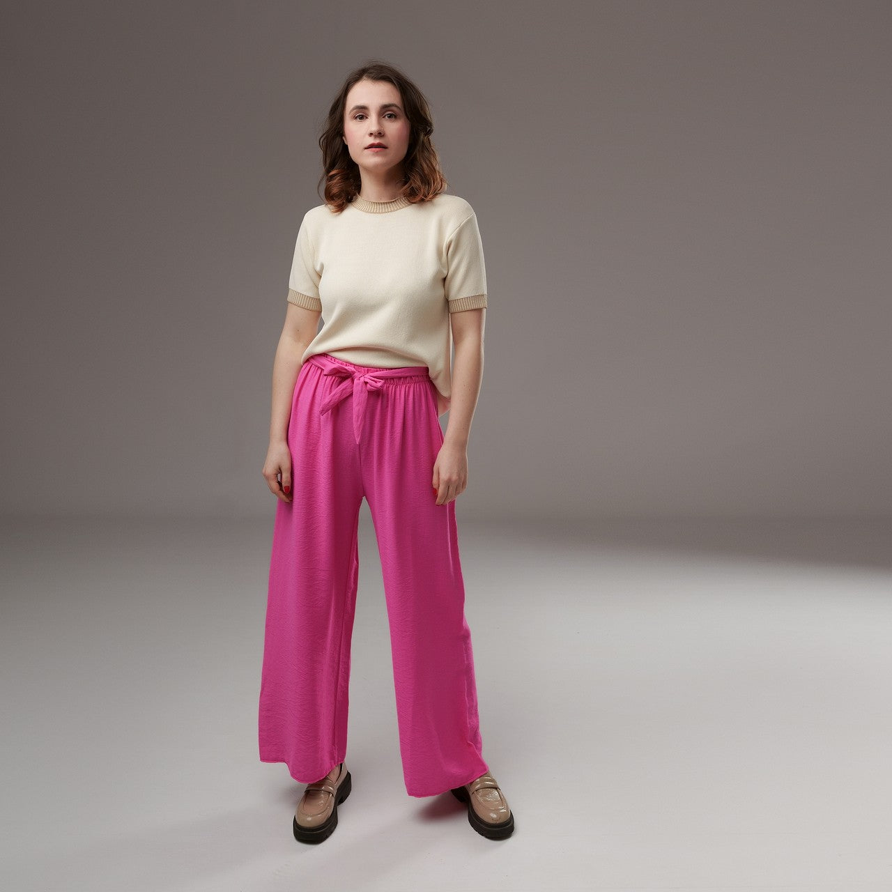 Pantaloni evazați din viscoză fucsia, talie elastică și cordon lat, model lejer, purtați cu un top crem, vedere frontală completă.