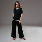 Ținută completă cu pantaloni evazați negri din viscoză și bluză neagră cu margini în dungi, purtată cu pantofi stiletto roșii.