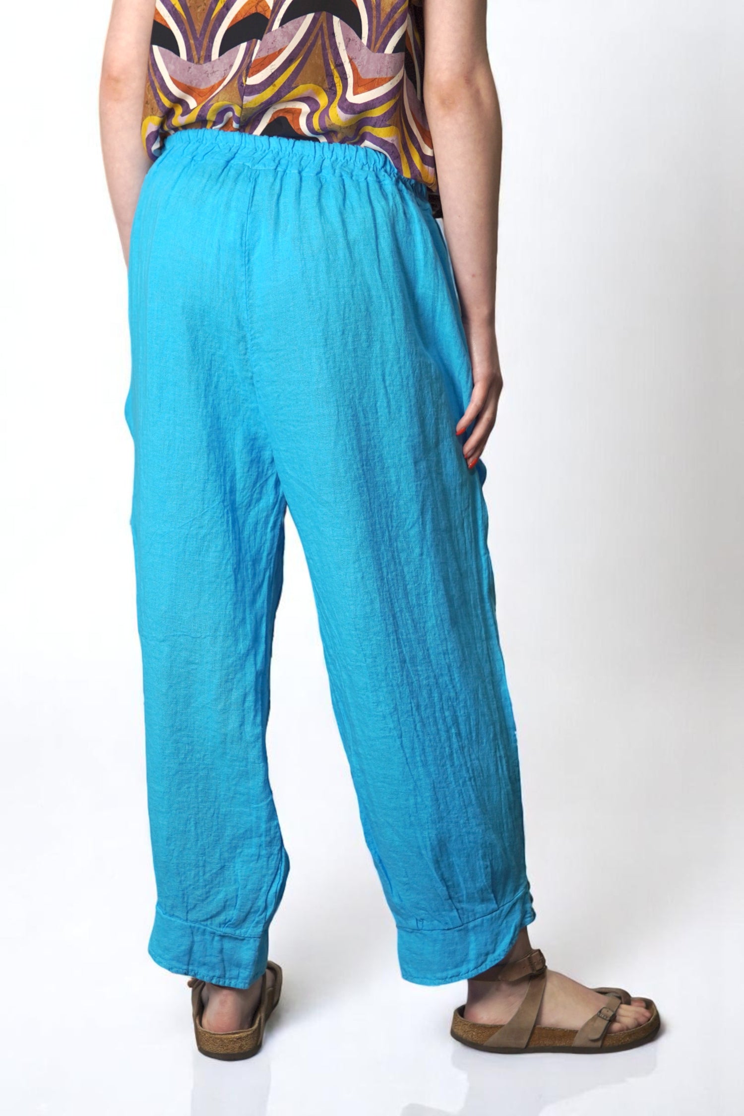 Vedere din spate a pantalonilor bleu din in, cu croială relaxată și finisaj larg la gleznă.