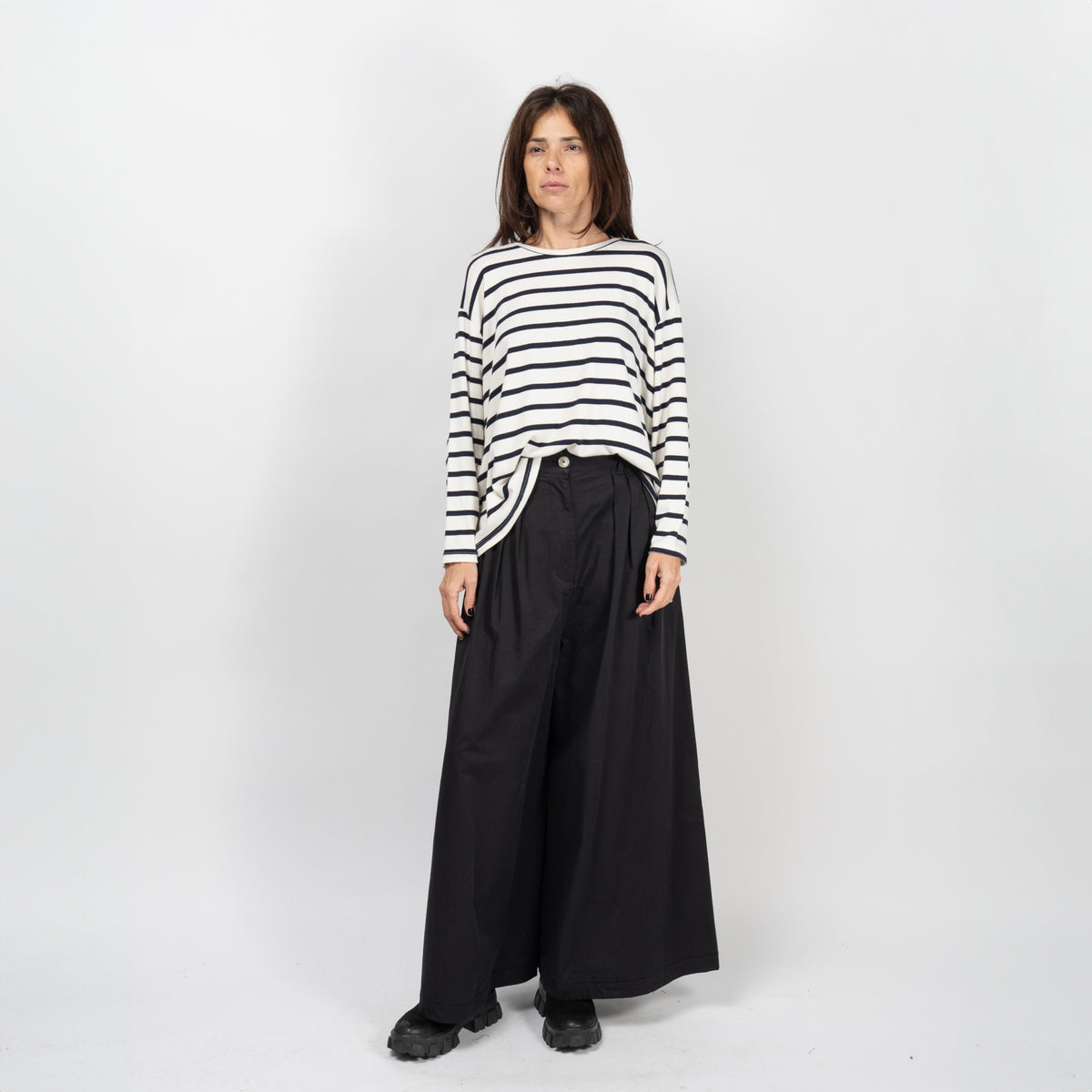 Model purtând pantaloni negri largi din bumbac structurat, stilizați cu un top cu dungi.