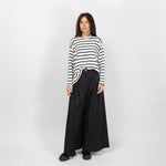 Model purtând pantaloni negri largi din bumbac structurat, stilizați cu un top cu dungi.