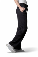 Vedere laterală a pantalonilor negri cu croială largă și talie cu șnur, purtați cu pantofi sport albi.