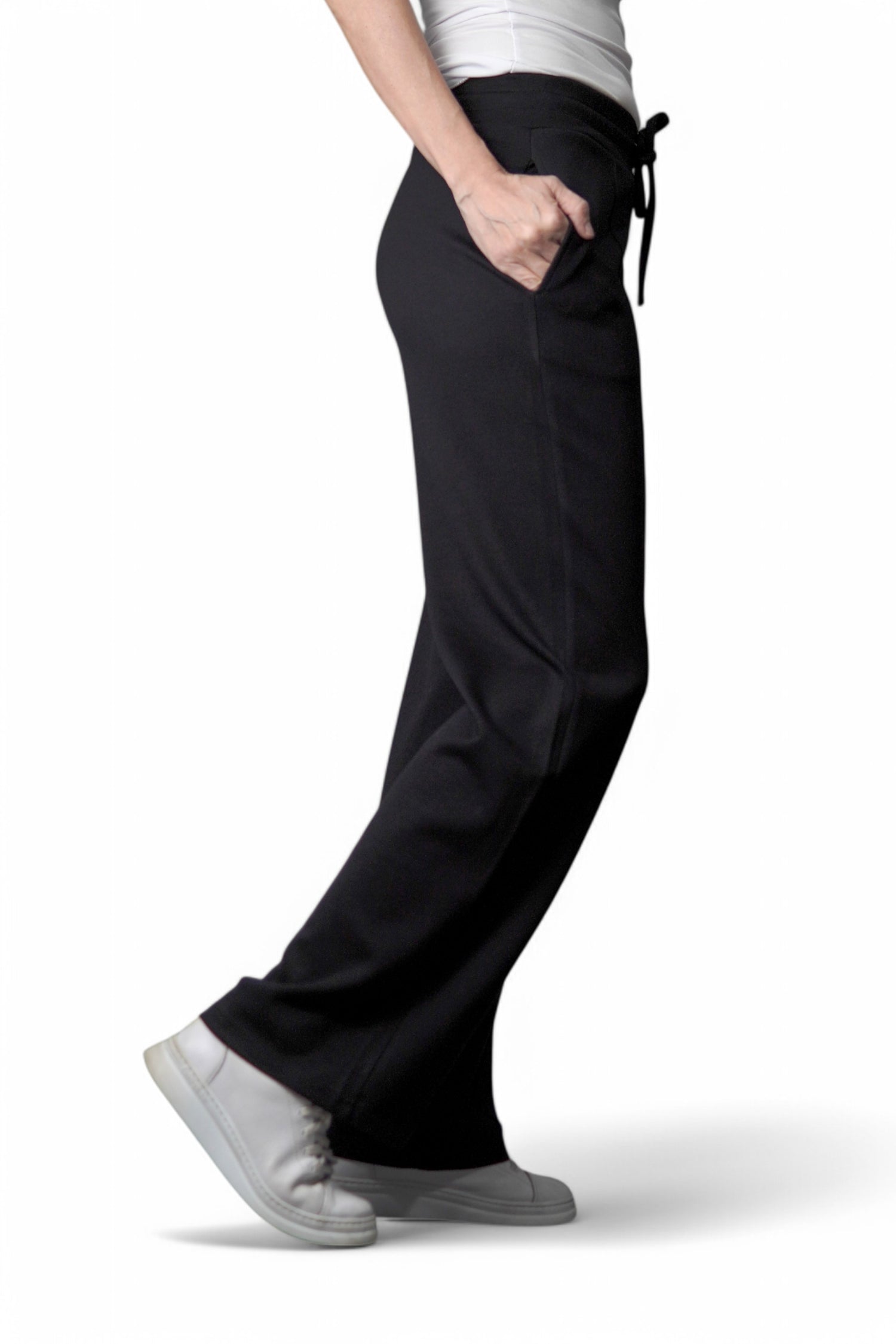 Vedere laterală a pantalonilor negri cu croială largă și talie cu șnur, purtați cu pantofi sport albi.