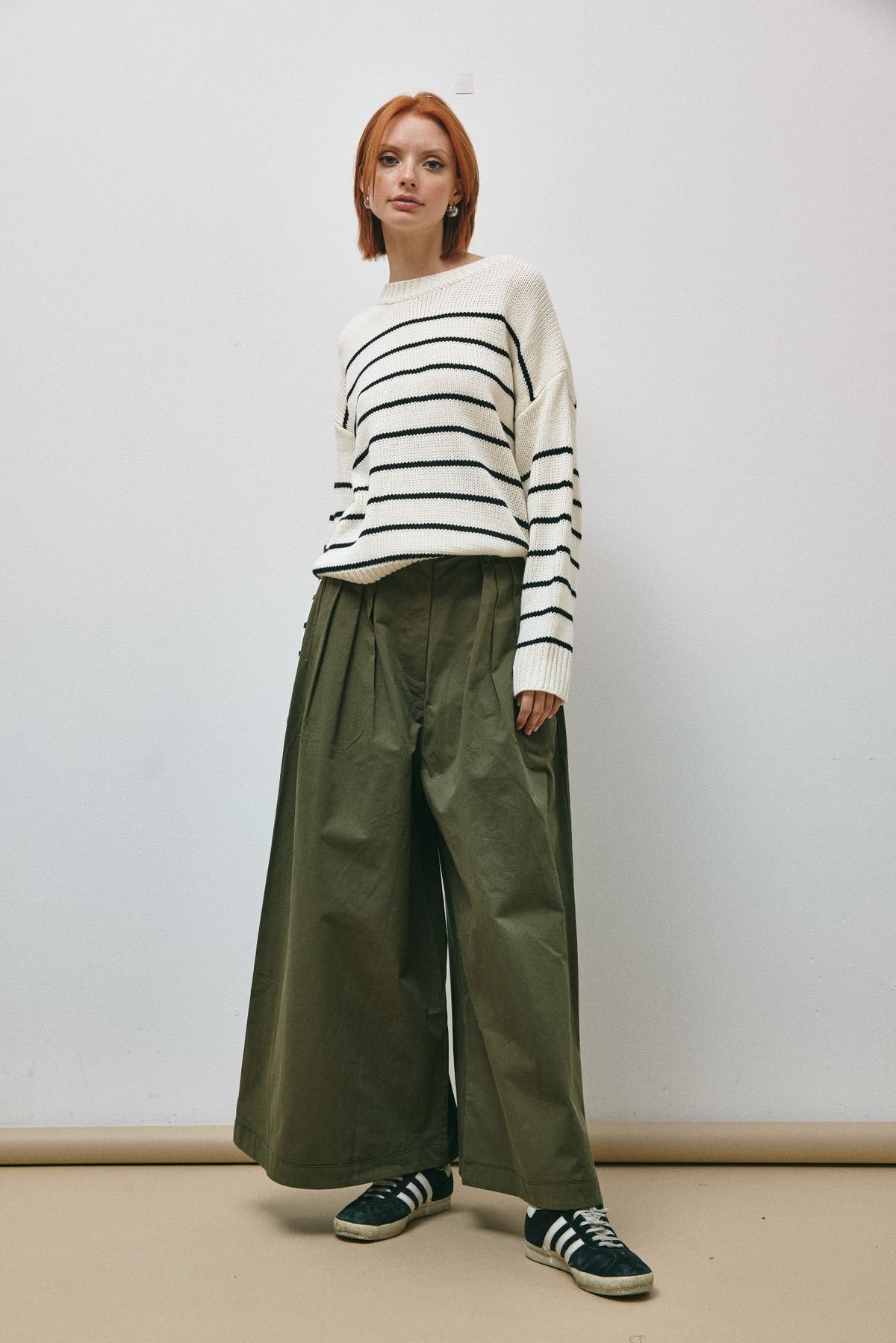  Model purtând pantaloni largi verde-oliv din bumbac structurat, asortați cu pulover în dungi.