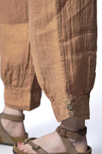 Detaliu al tivului pantalonilor din in maro, cu trei nasturi decorativi pe gleznă.