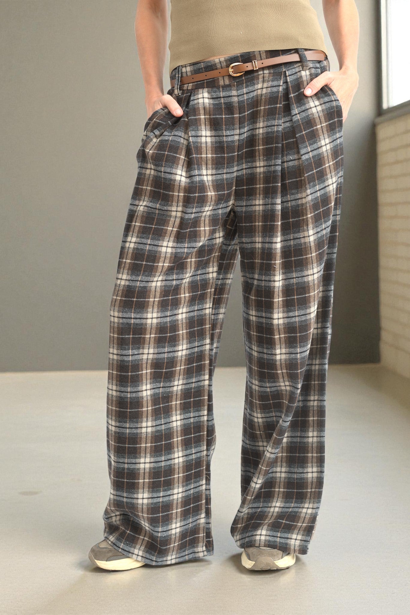 Pantaloni drepți din stofă în carouri maro-bej, purtați cu talia evidențiată de o curea subțire maro.