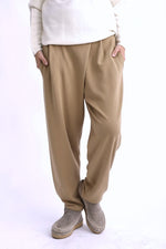 Pantaloni tip trening conici bej, cu pliuri la talie și croială lejeră, purtați pe model, vedere din față.