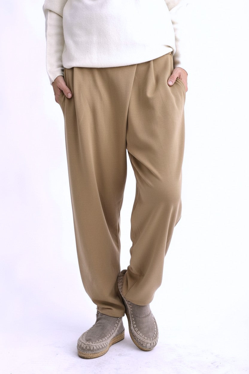 Pantaloni tip trening conici bej, cu pliuri la talie și croială lejeră, purtați pe model, vedere din față.