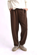 Pantaloni conici maro, tip trening elegant, cu pliuri frontale și talie elastică, purtați pe model.