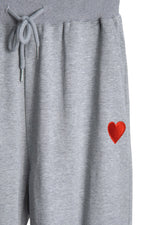 Detaliu al materialului pantalonilor de trening gri, evidențiind broderia inimii roșii.