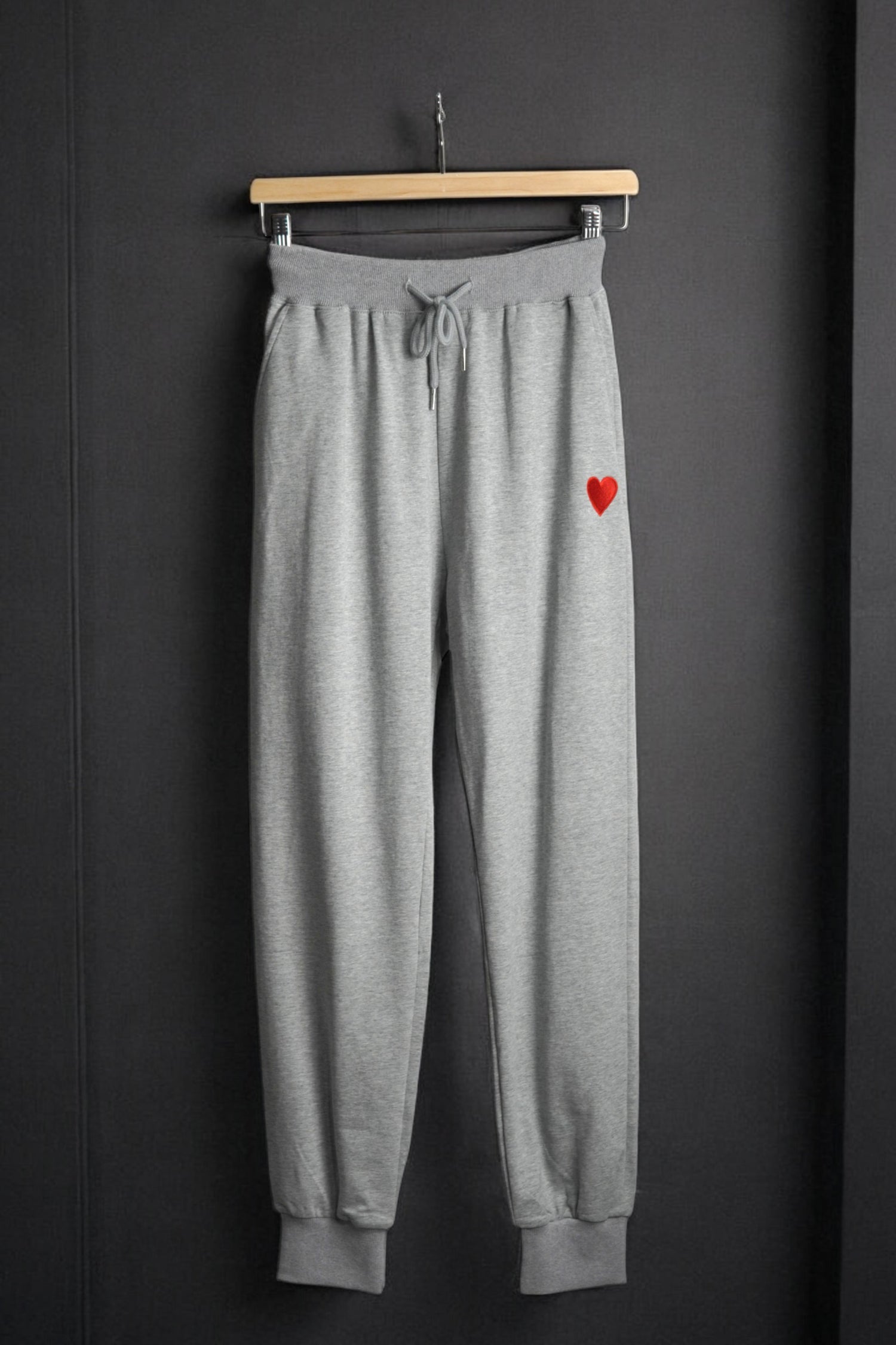 Pantaloni de trening gri cu talie elastică și șnur, decorați cu o inimă roșie brodată pe piciorul stâng.