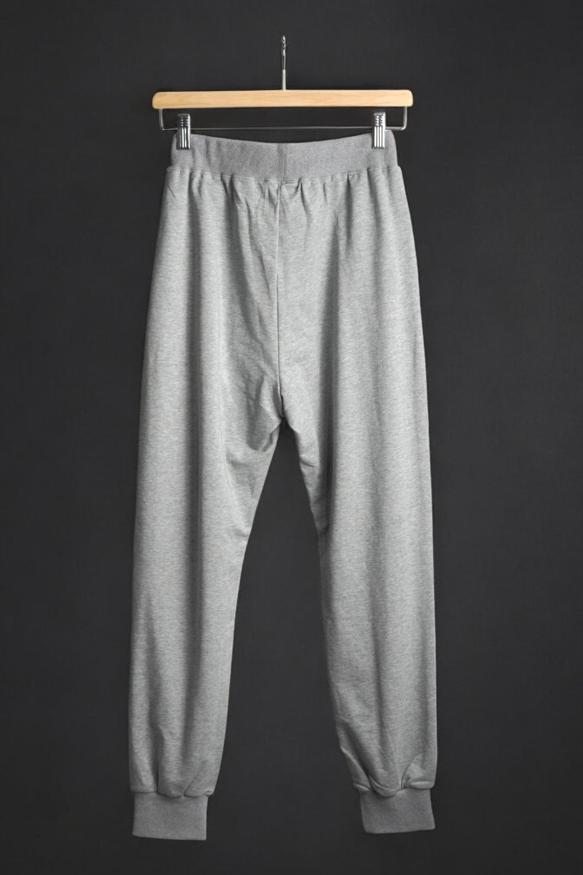 Vedere din spate a pantalonilor de trening gri, cu croială lejeră și elastic la gleznă.