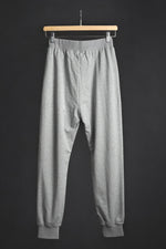 Vedere din spate a pantalonilor de trening gri, cu croială lejeră și elastic la gleznă.