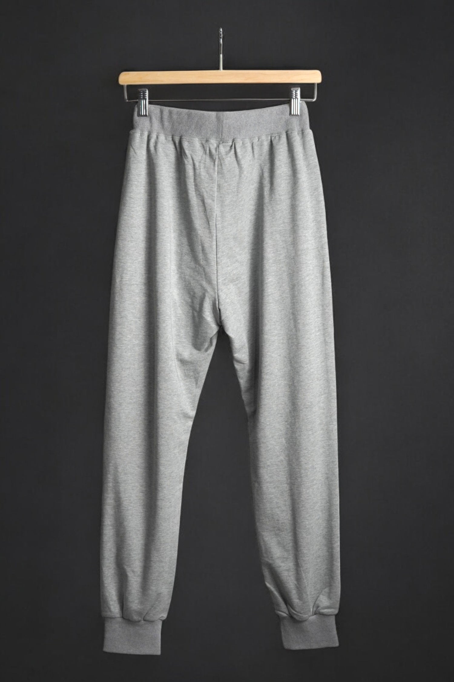 Vedere din spate a pantalonilor de trening gri, cu croială lejeră și elastic la gleznă.