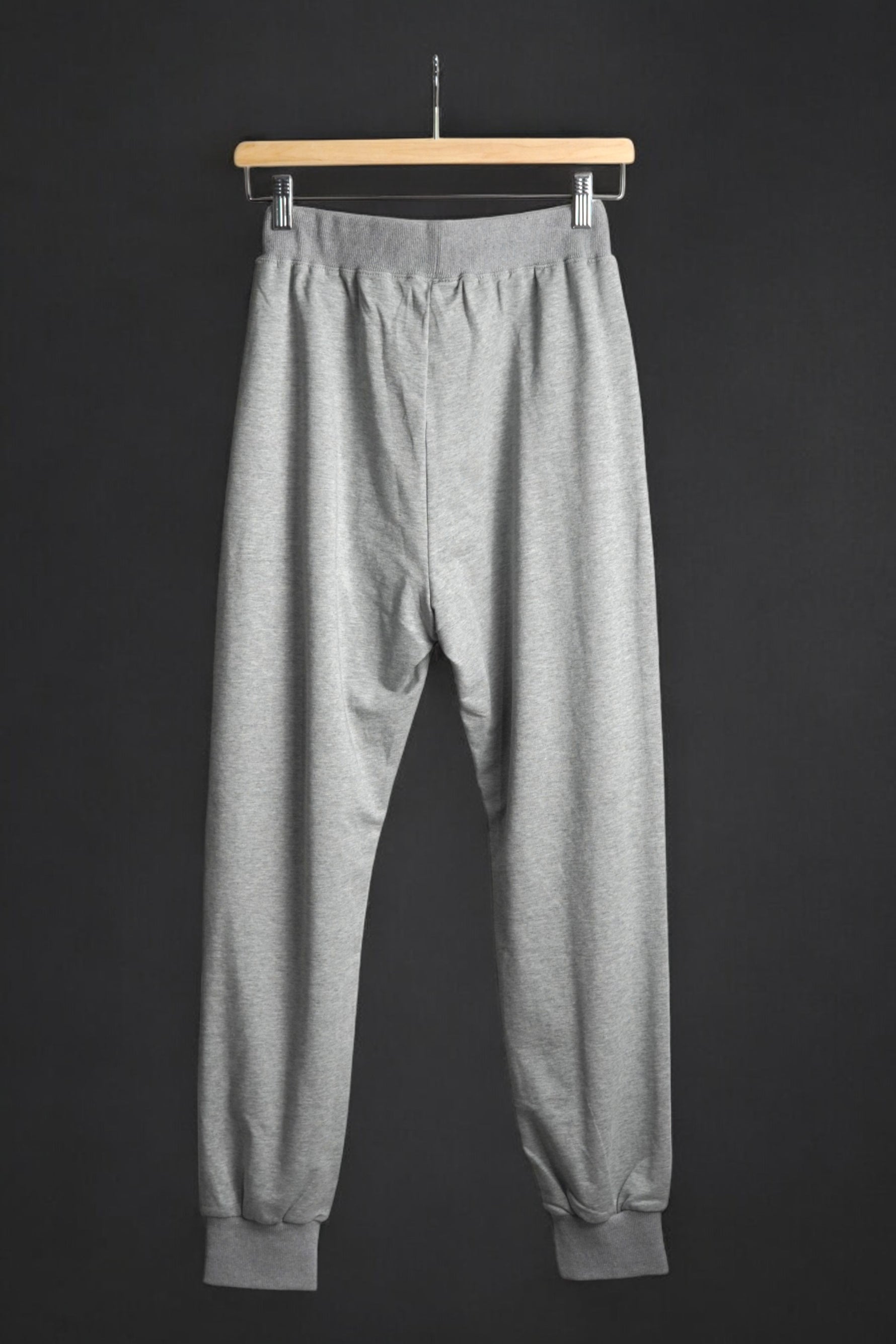 Vedere din spate a pantalonilor de trening gri, cu croială lejeră și elastic la gleznă.