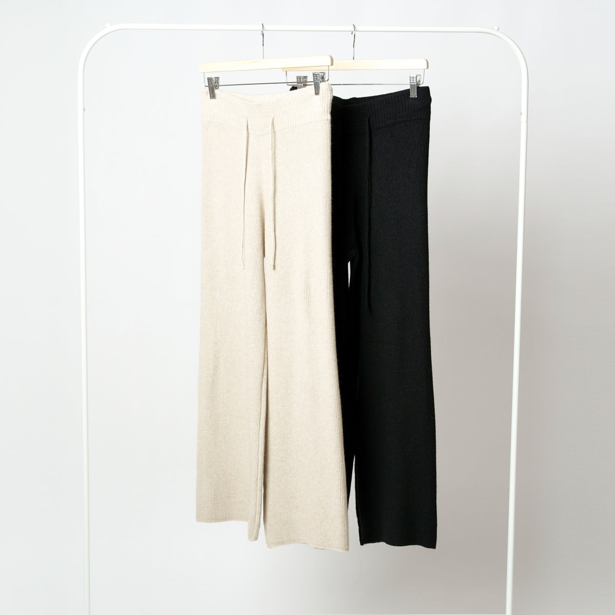 Pantaloni din tricot soft prezentați pe umeraș, culori bej și negru, material flexibil cu striații.