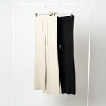 Pantaloni din tricot soft prezentați pe umeraș, culori bej și negru, material flexibil cu striații.