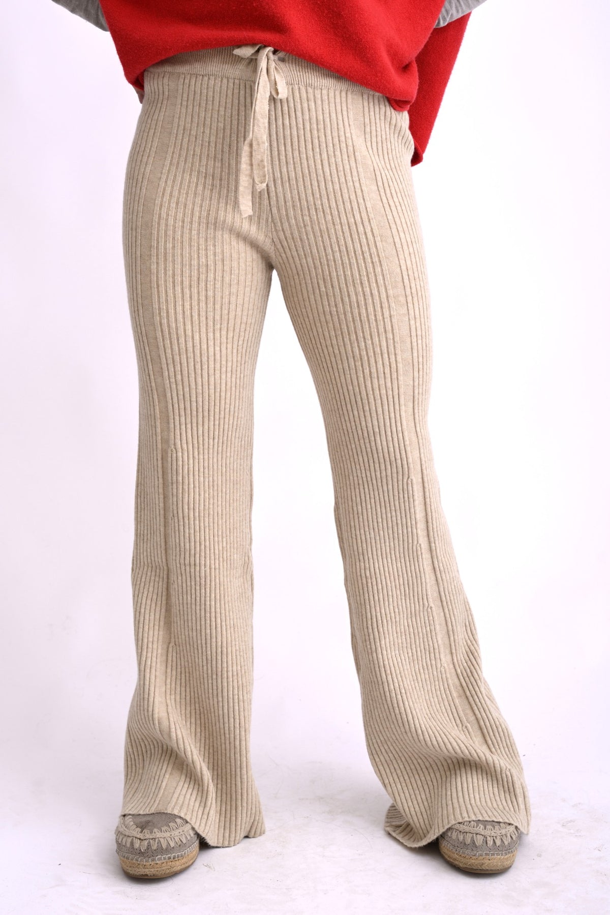 Model poartă pantaloni tricotați bej, cu model ajurat și talie elastică, croială lejeră evazată.