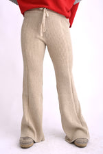 Model poartă pantaloni tricotați bej, cu model ajurat și talie elastică, croială lejeră evazată.