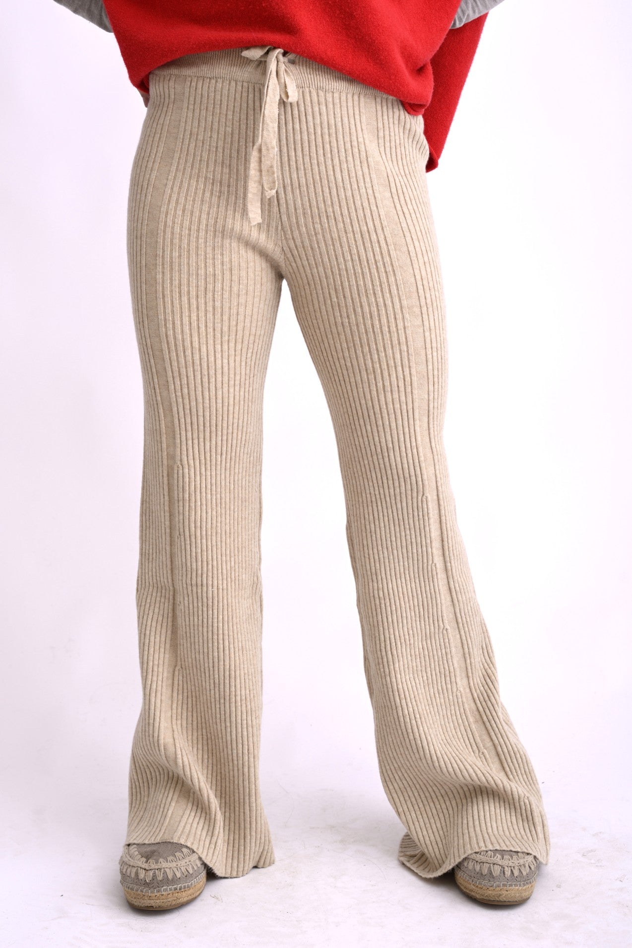 Model poartă pantaloni tricotați bej, cu model ajurat și talie elastică, croială lejeră evazată.