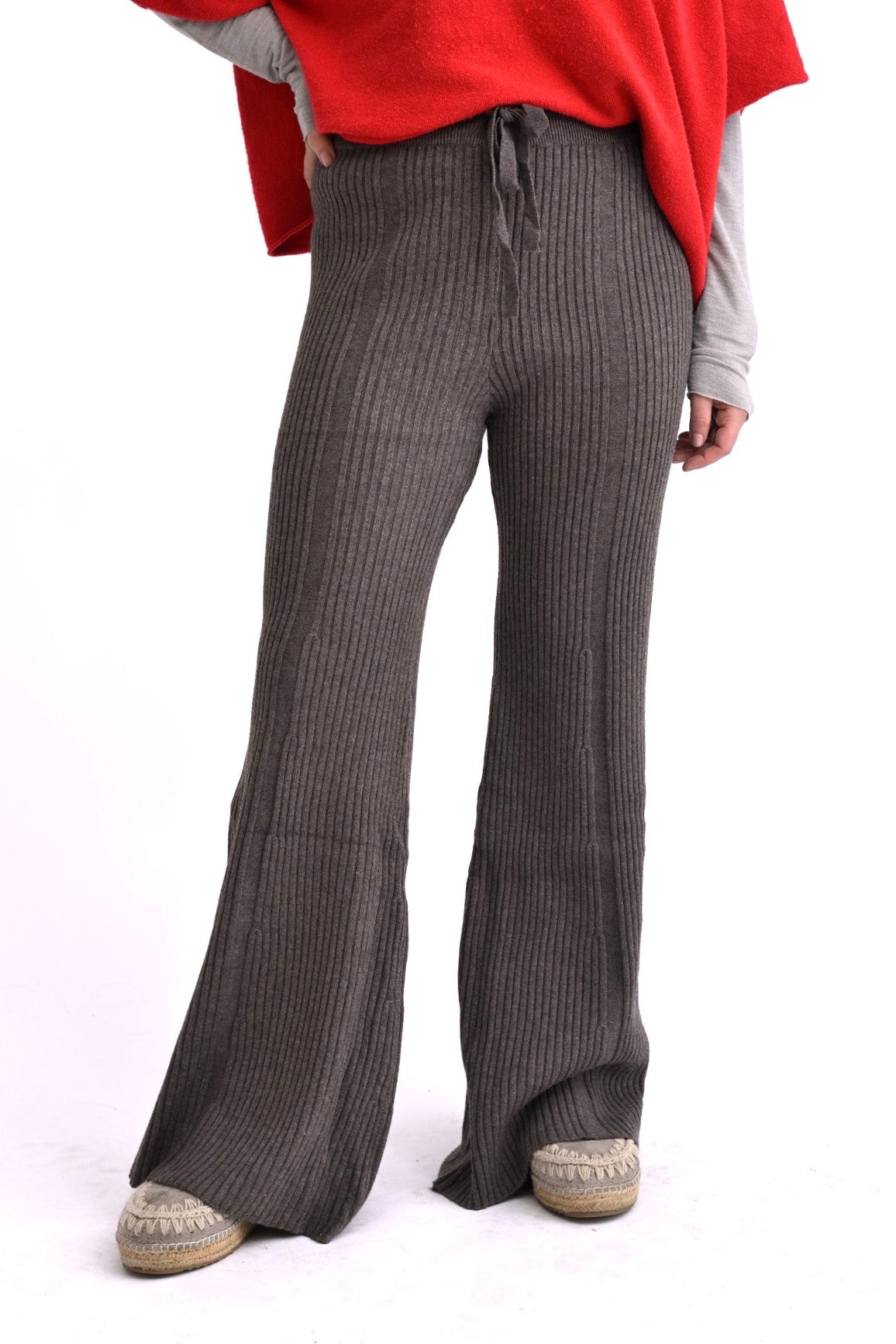 Model poartă pantaloni tricotați cafenii, cu model ajurat și croială evazată, talie elastică, pe fundal alb.