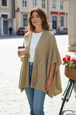 Pelerină tricotată bej, purtată peste un tricou alb și blugi, cu croială lejeră și textură fină, ideală pentru ținute casual de toamnă.