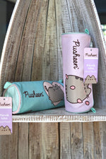 Două penare tip tubă cu Pusheen, în culorile lila și verde mentă, cu fermoar și etichetă „Pencil Pouch”, pe raft din lemn.
