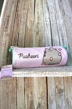 Penar tip tubă Pusheen, culoare lila, imprimeu cu pisica Pusheen, fermoar, așezat pe raft din lemn.