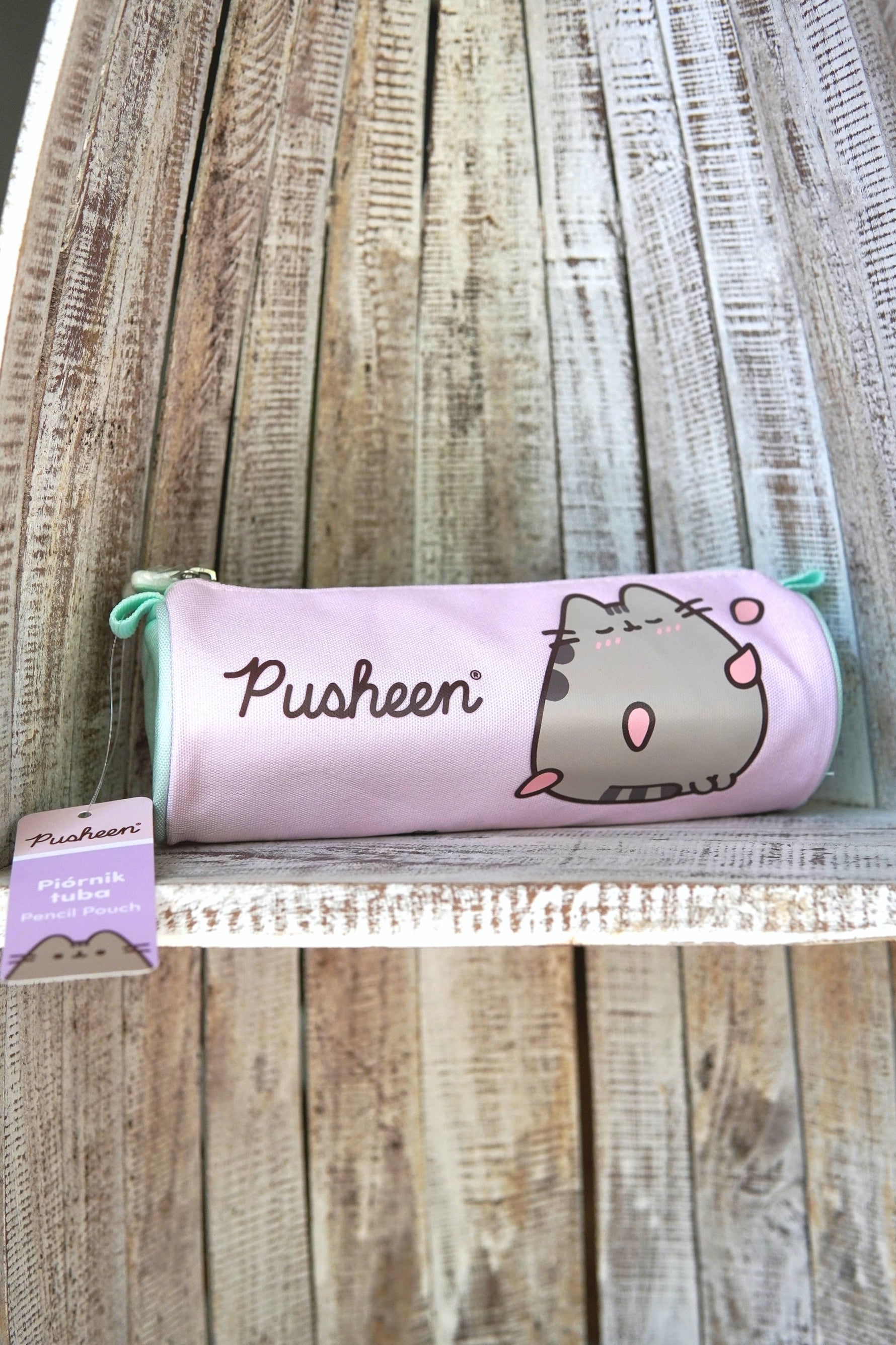 Penar tip tubă Pusheen, culoare lila, imprimeu cu pisica Pusheen, fermoar, așezat pe raft din lemn.