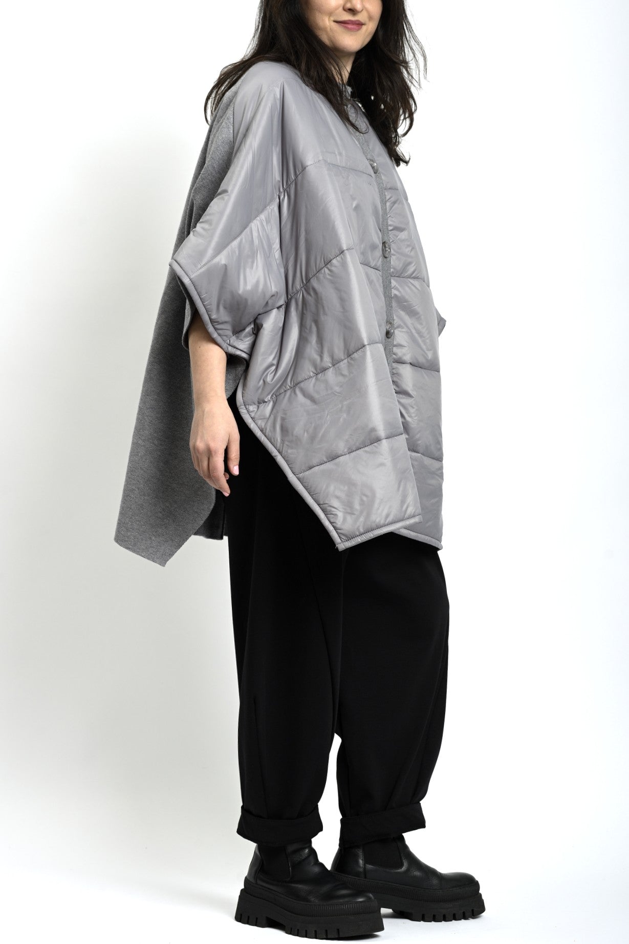 Vedere laterală a ponchoului gri din tricot matlasat, cu cădere amplă și mâneci largi.