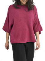 Pulover oversize din amestec cu alpaca, nuanță roz zmeură, cu mânecă scurtă și croială amplă, purtat cu pantaloni negri.