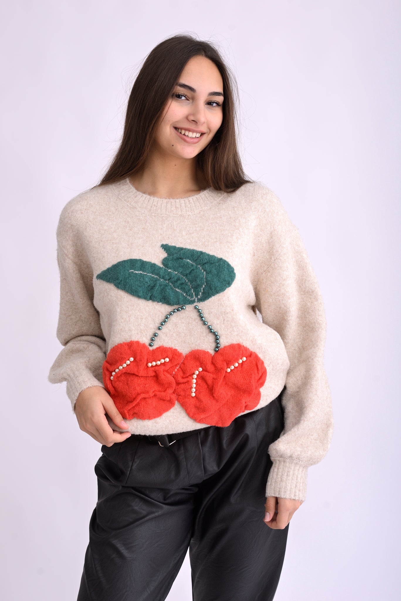 Detaliu de material tricotat bej cu aplicații tricotate în formă de cireșe și perle decorative.