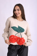 Pulover tricotat bej cu detalii cireșe roșii și frunze verzi, croială lejeră, vedere laterală pe model.