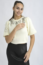 Pulover cu mânecă scurtă și aplicații decorative pe umeri, într-o nuanță delicată de crem.
