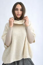 Pulover bej pufos pentru femei, cu guler mare și croială lejeră, purtat cu fustă gri.