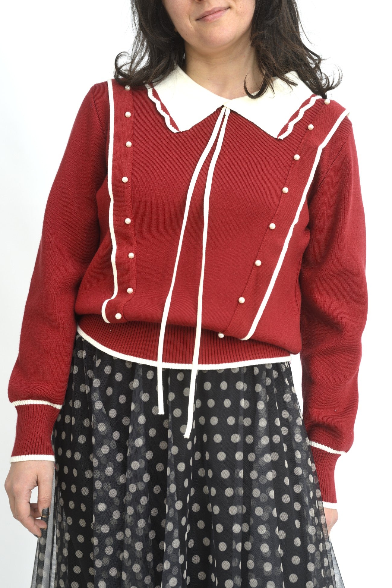 Prim-plan cu puloverul roșu, textura tricotată și șnururile lungi decorative.