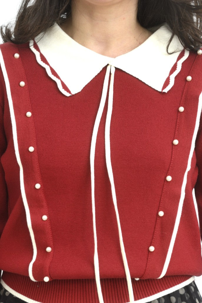 Detaliu al gulerului ondulat în contrast alb-roșu, cu șnururi lungi decorative.