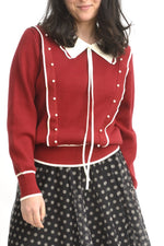 Pulover roșu cu guler ondulat alb și șnururi lungi decorative, prezentat frontal pe model.