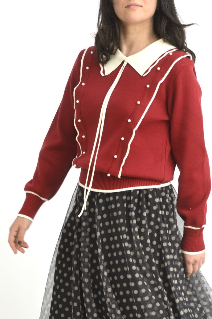 Pulover roșu cu guler ondulat și șnururi lungi, fotografiat din lateral pentru a evidenția croiala lejeră.