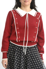 Pulover roșu cu detalii albe și guler ondulat, prezentat din spate pe model.