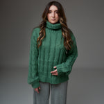 Pulover verde împletit cu torsade dese, guler înalt și croială dreaptă, văzut din față