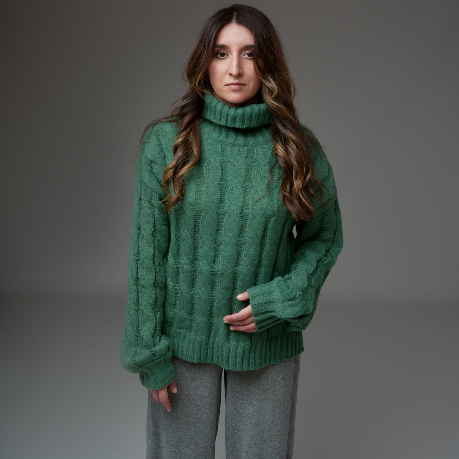 Pulover verde împletit cu torsade dese, guler înalt și croială dreaptă, văzut din față