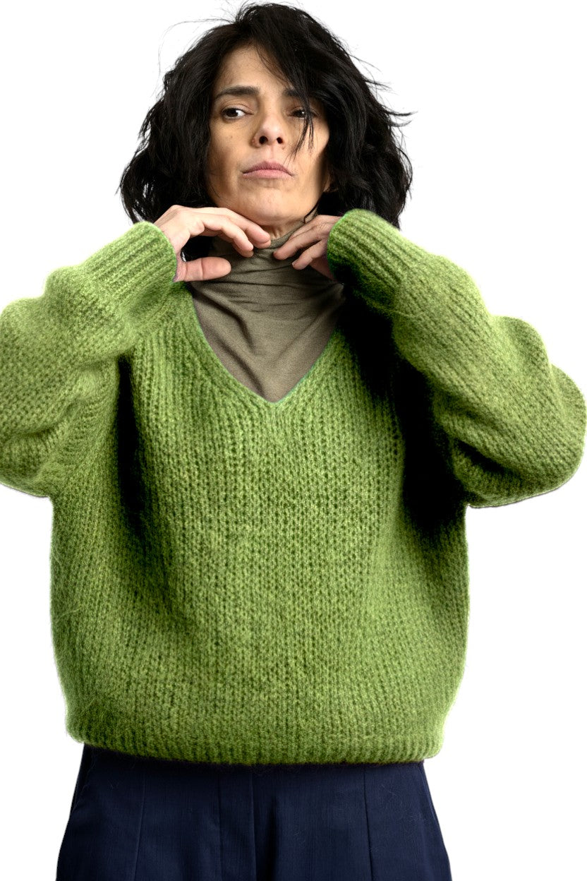 Pulover pufos din mohair, verde, cu decolteu în V și croială lejeră, purtat peste helancă, vedere din față.