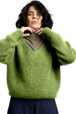 Pulover pufos din mohair, verde, cu decolteu în V și croială lejeră, purtat peste helancă, vedere din față.