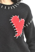 Detaliu de guler la puloverul negru, cu cusături albe contrastante în jurul decolteului.