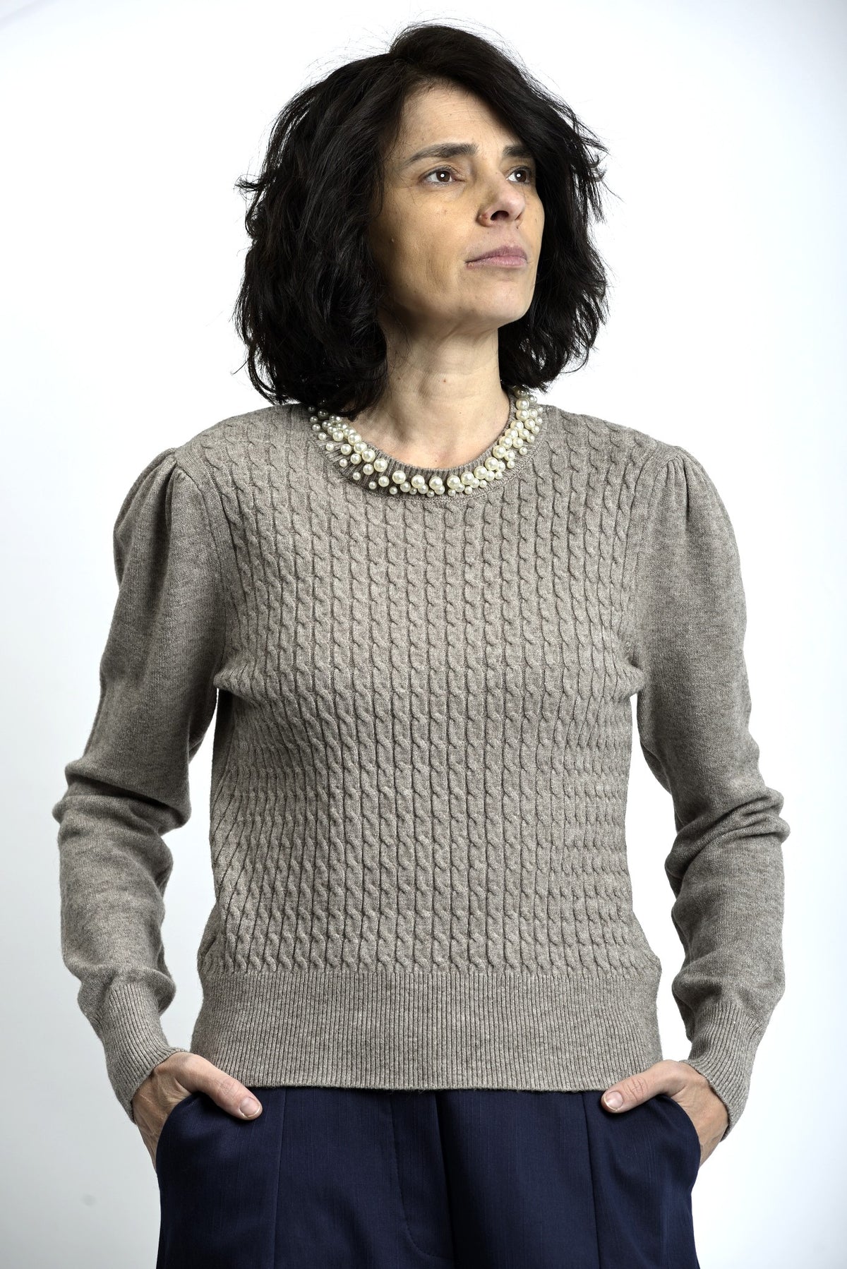 Detaliu colier cu perle aplicat la baza gulerului unui pulover tricotat cu torsade.