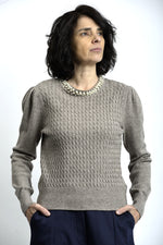 Detaliu colier cu perle aplicat la baza gulerului unui pulover tricotat cu torsade.