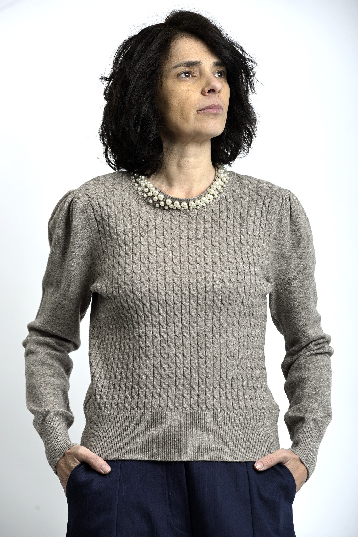 Detaliu colier cu perle aplicat la baza gulerului unui pulover tricotat cu torsade.