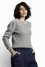 Vedere laterală a puloverului cu torsade și colier decorativ cu perle, evidențiind textura tricotului.